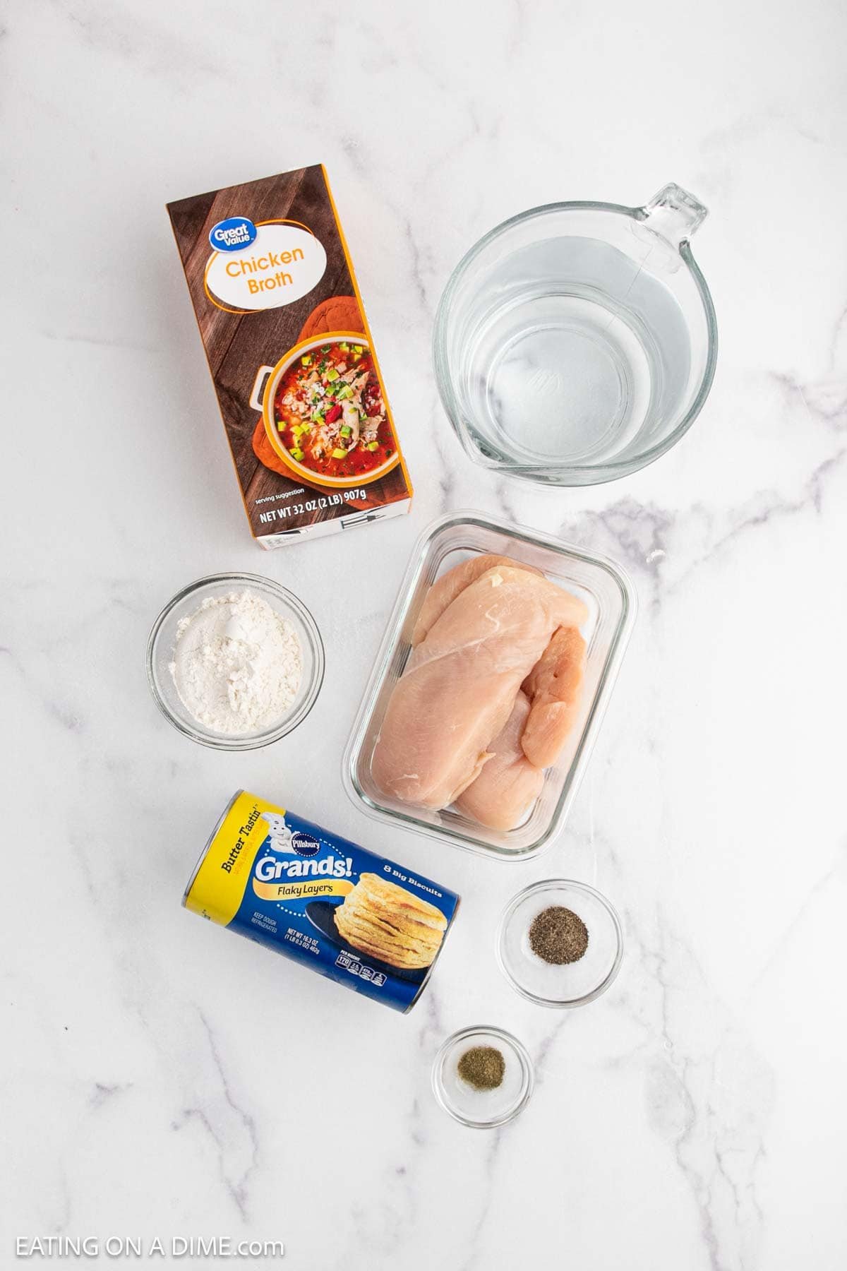 Top-down view of Chicken and Biscuits ingredients on a marble surface: chicken broth, water, raw chicken breasts, Grands! biscuits, flour, and small bowls of salt and pepper. Perfect for making classic Chicken and Dumplings.