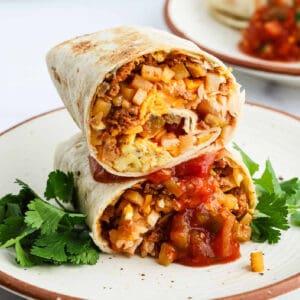 A Chorizo Breakfast Burrito cut in half, filled with scrambled eggs, potatoes, cheese, and salsa, garnished with fresh cilantro on a white plate.