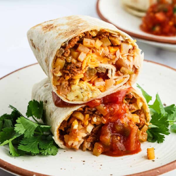 A Chorizo Breakfast Burrito cut in half, filled with scrambled eggs, potatoes, cheese, and salsa, garnished with fresh cilantro on a white plate.