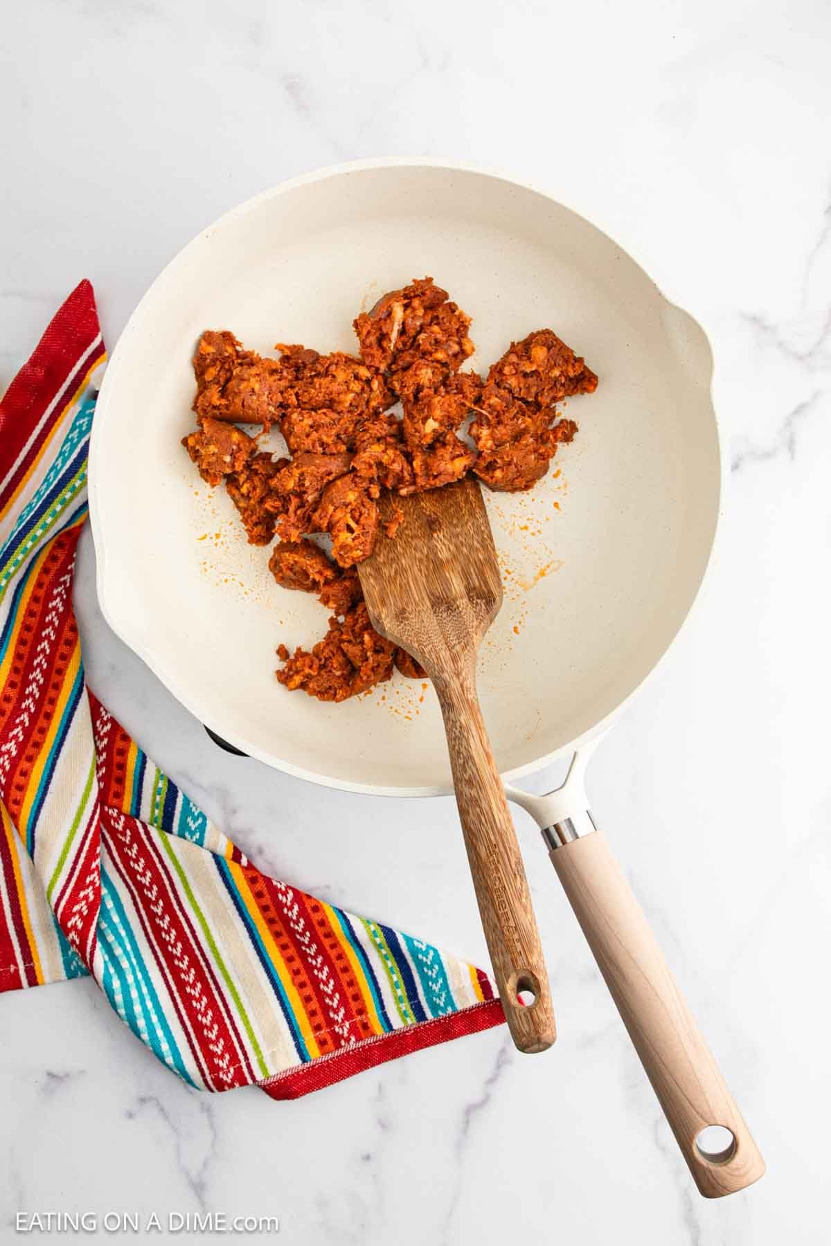 Cooking chorizo in a skillet with a wooden spoon