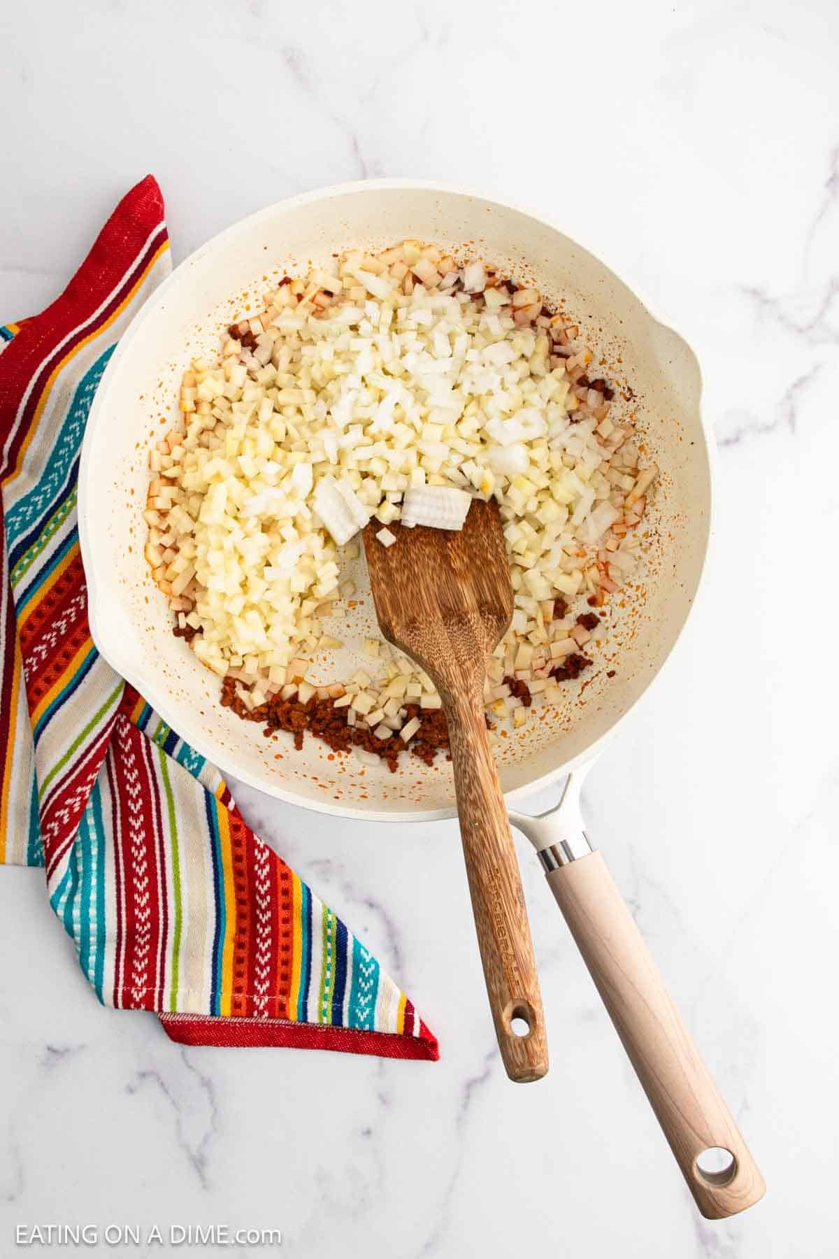 Cooking diced onions and potatoes in a skillet with a wooden spoon
