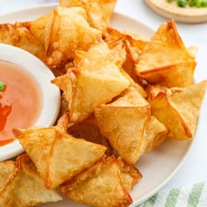 A plate of golden-brown Cream Cheese Wontons arranged around a bowl of sweet and sour dipping sauce, ready to be served.