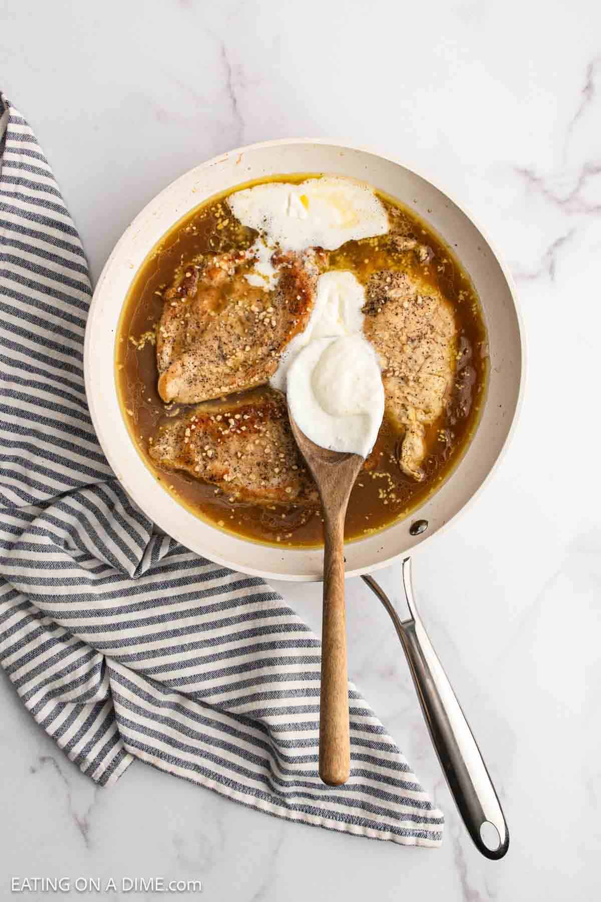 Spooning the heavy cream mixture into the skillet with chicken and the broth