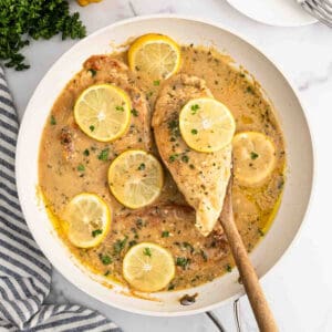 Lemon chicken in a white saucepan with a wooden spoon.