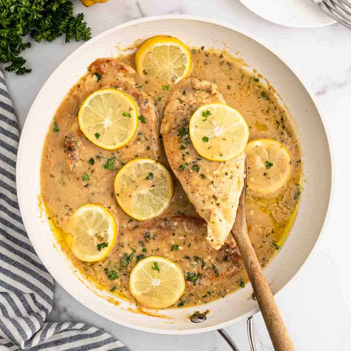Lemon chicken in a white saucepan with a wooden spoon.