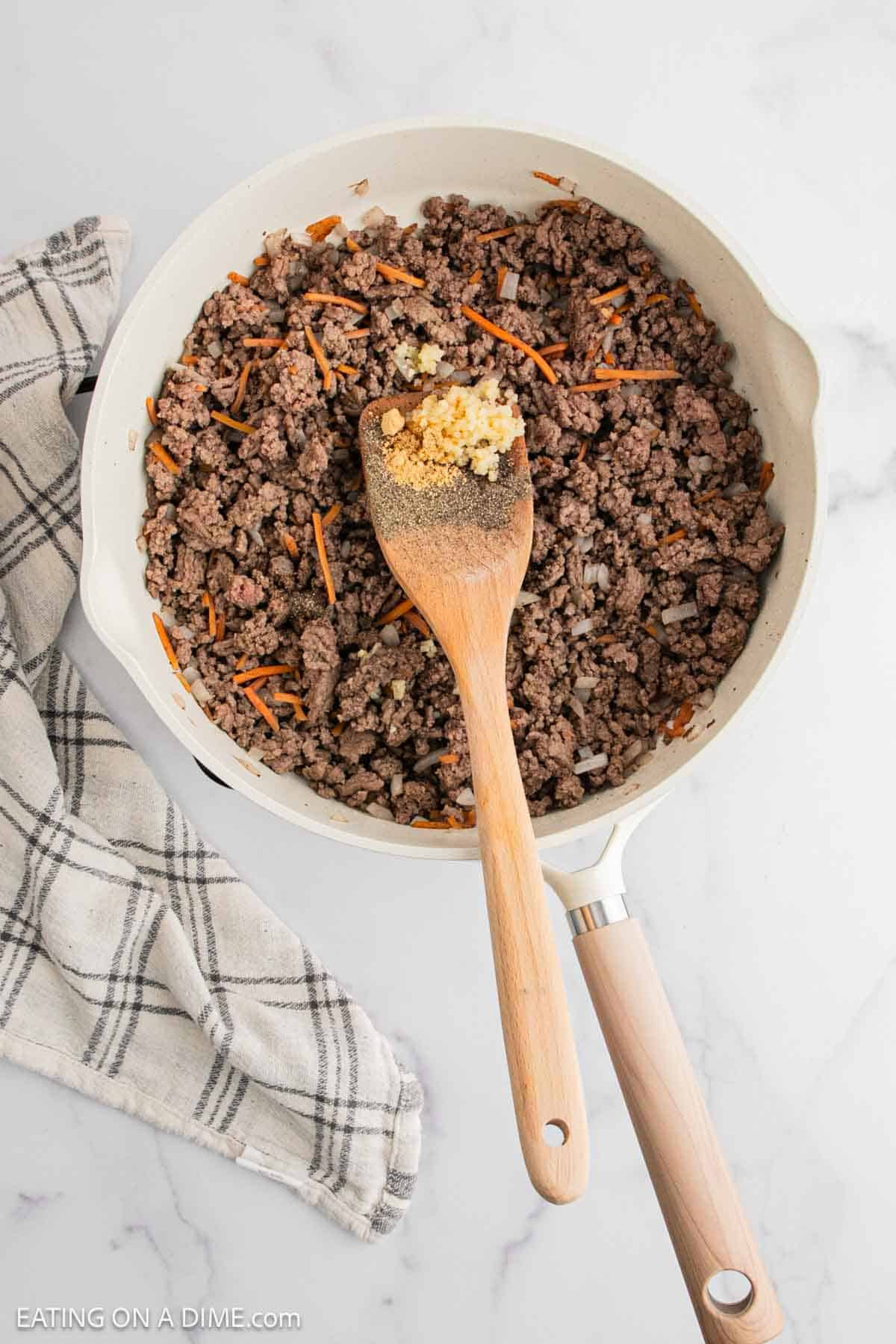 Cooked ground beef with shredded carrots and minced garlic and black pepper on the wooden spoon
