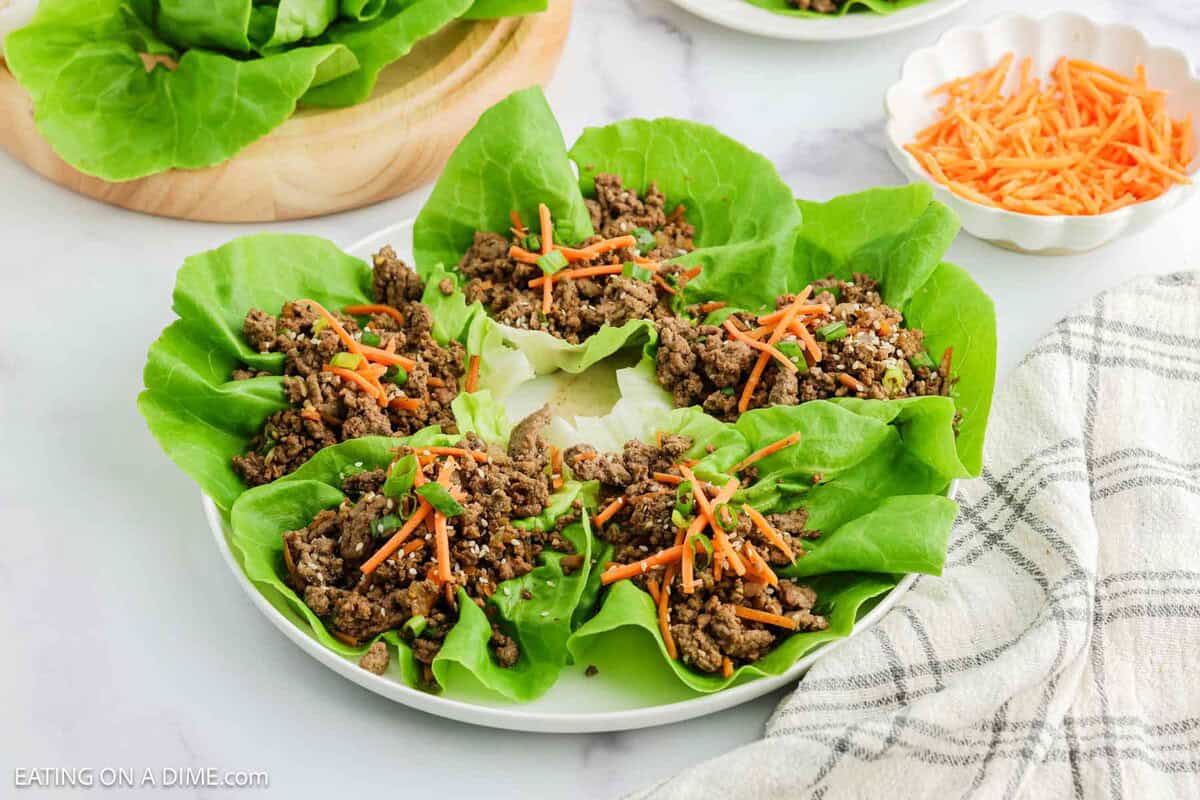 Lettuce wraps on a plate with a small bowl of shredded carrots on the side