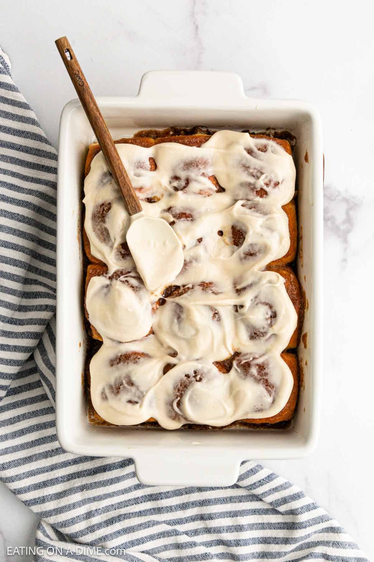 Spreading the cream cheese frosting over the cinnamon rolls in the baking dish