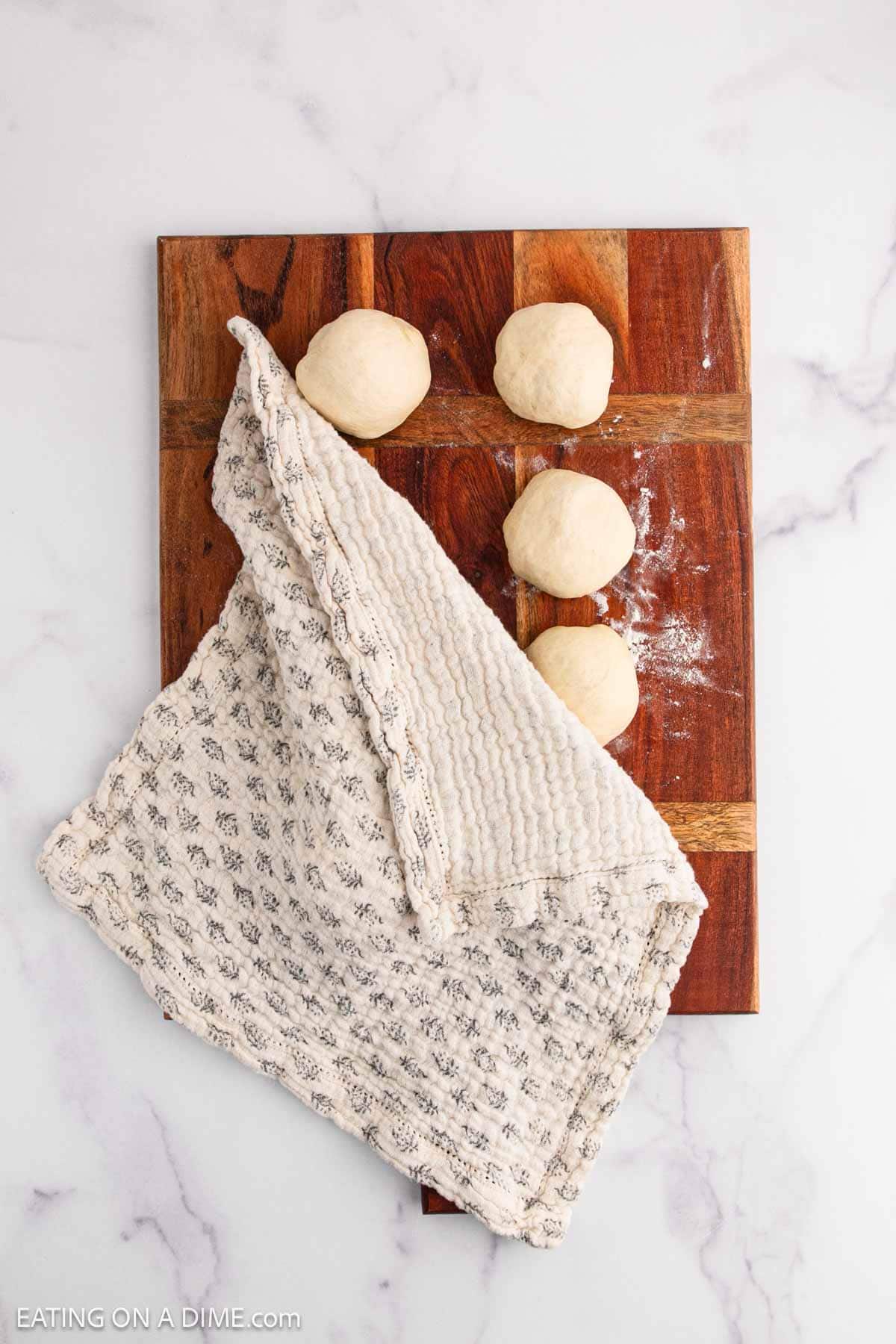 Dough balls on a piece of wooden platter covered with kitchen towel