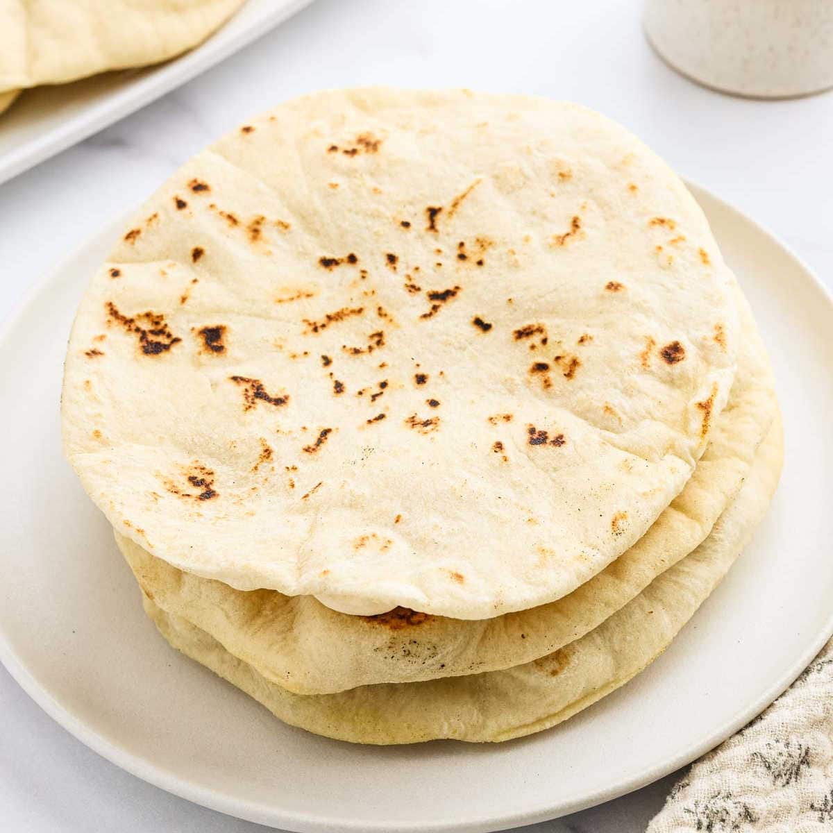 Three flatbreads stacked on a white plate.