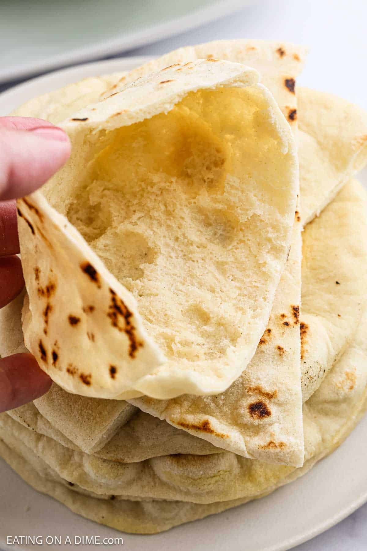 Pita bread stacked on a plate with the pita bread pocket showing