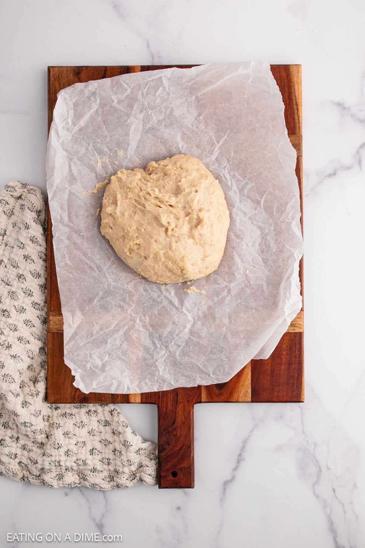 Dough on a piece of parchment paper on wooden platter