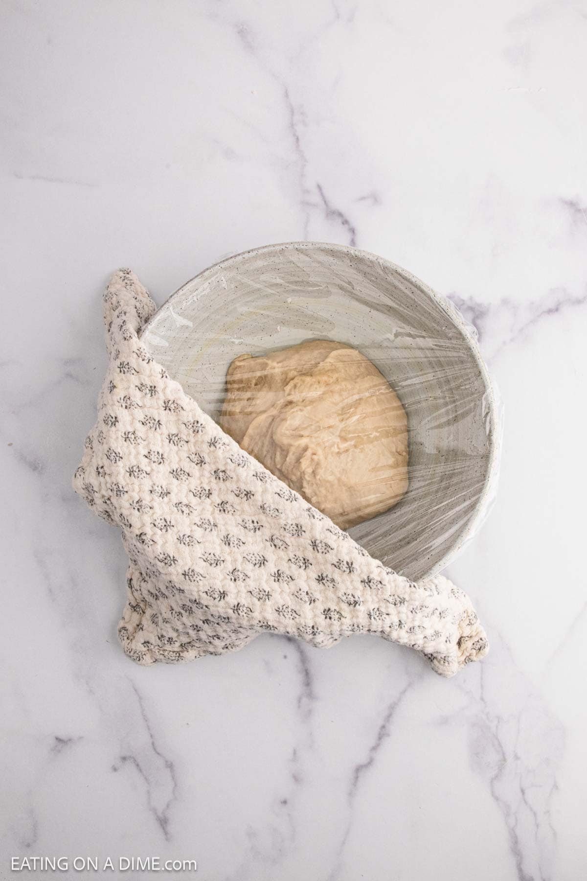 Dough ball in a bowl covered with plastic wrap topped with a towel
