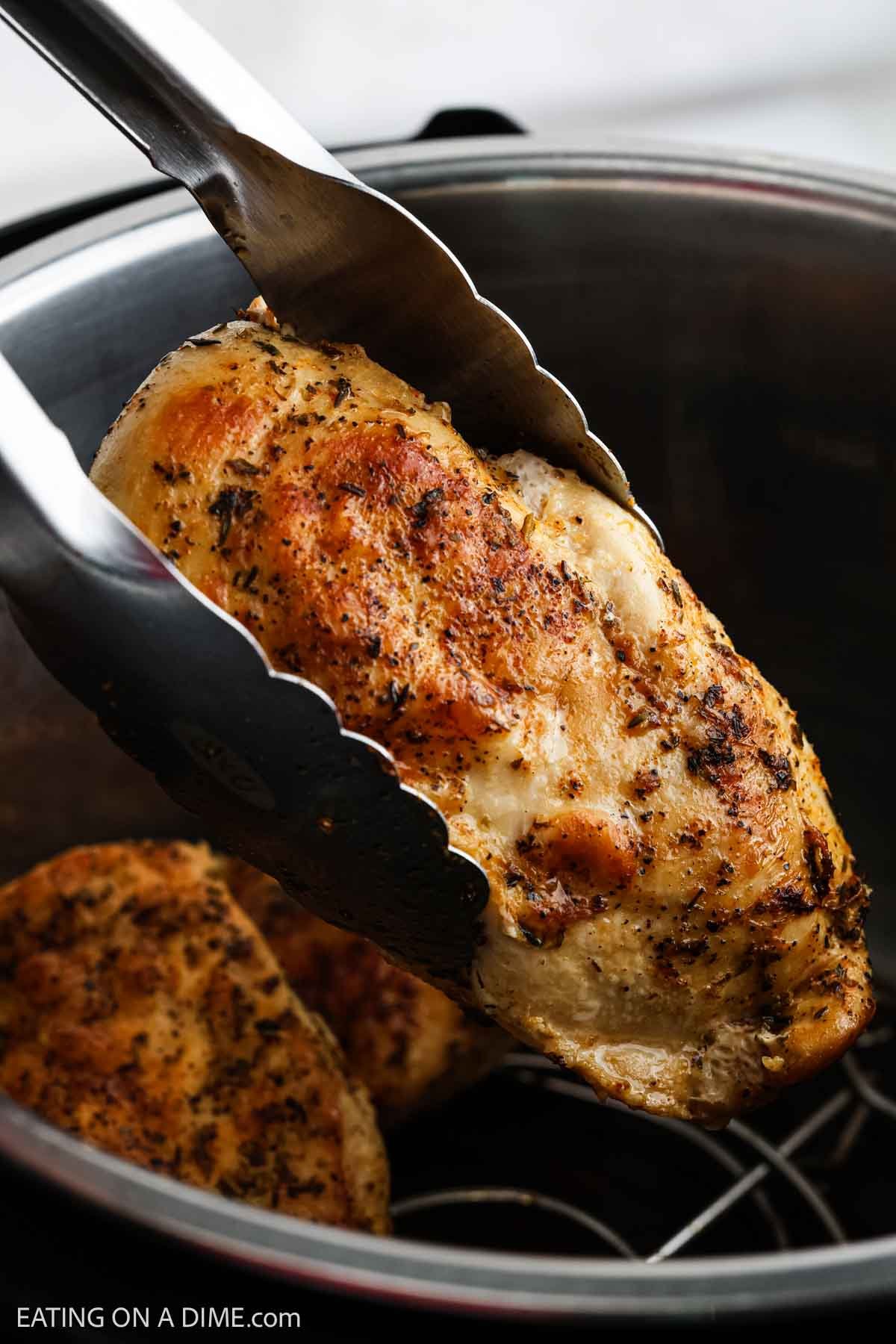 Cooked chicken breast being held by silver tongs