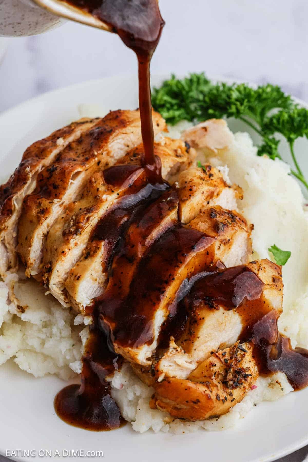 Cooked chicken breast with BBQ Sauce being poured over the top served with mashed potatoes