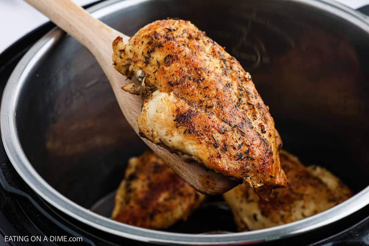 Golden Brown Chicken Breast on a wooden spoon over the instant pot