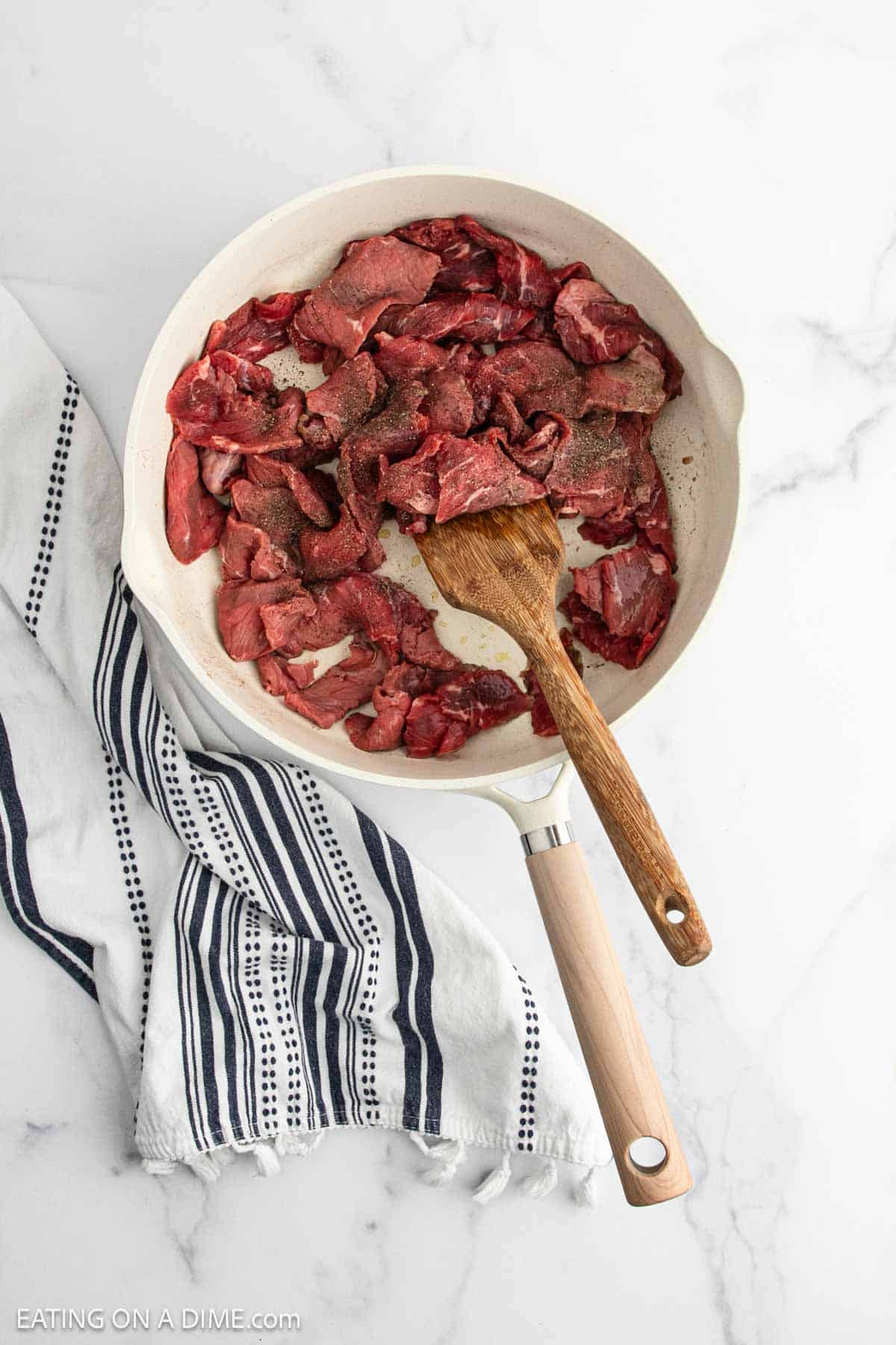 Strips of steak in the skillet with a wooden spoon
