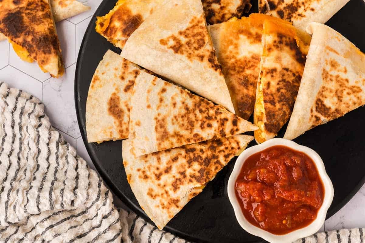 Breakfast Quesadillas cut into wedges stacked on a black plate with a small bowl of salsa on the side