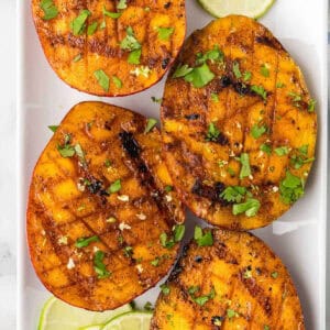 Grilled peaches with lime slices on a white plate.