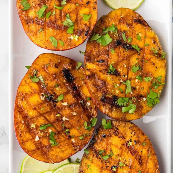 Grilled peaches with lime slices on a white plate.