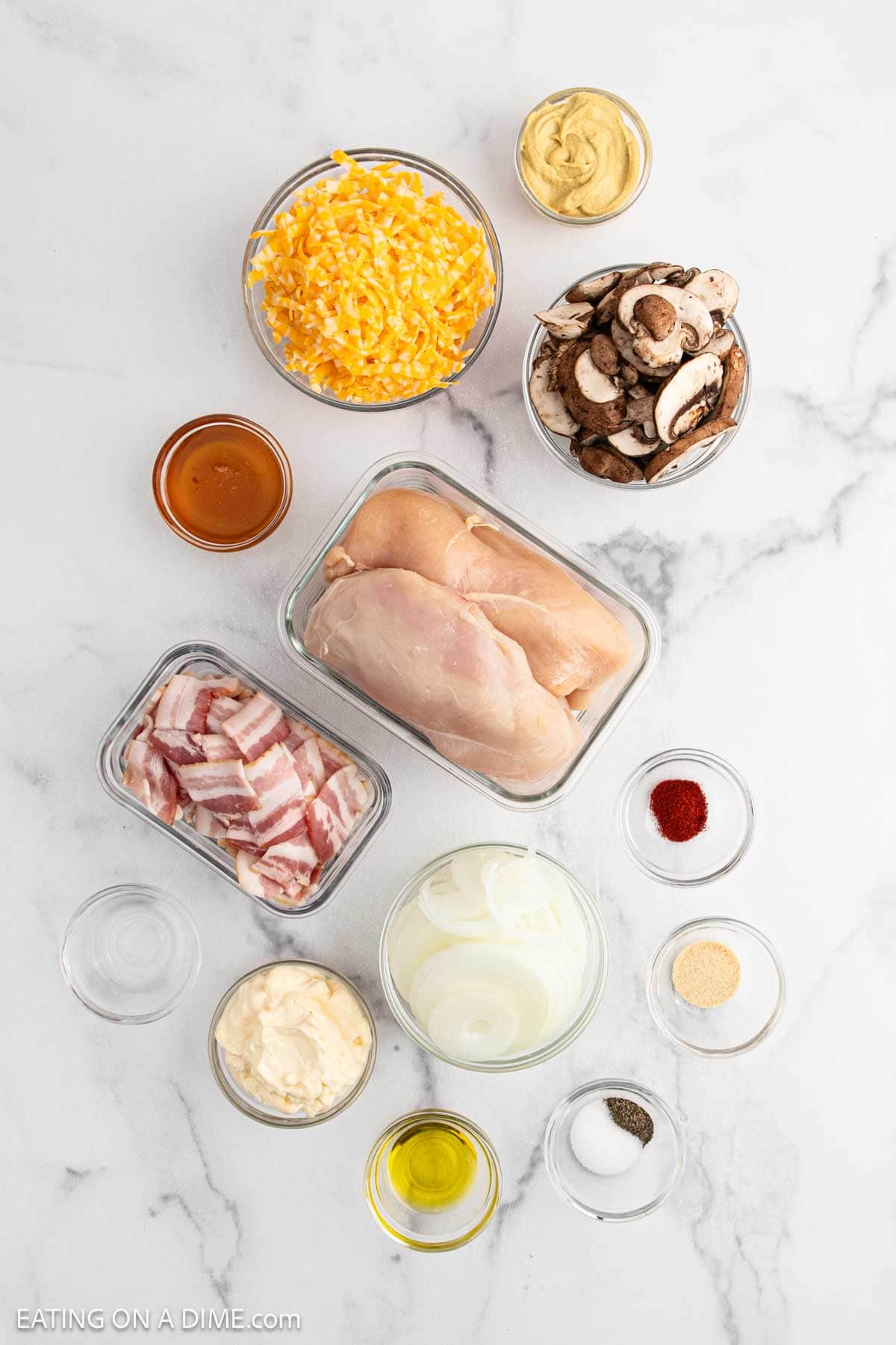 A marble surface with bowls of shredded cheese, sliced mushrooms, onions, raw chicken breasts, bacon, mustard, mayonnaise, oil, honey, and seasoningsโeverything you need to make Alice Springs Chicken inspired by the famous Outback Steakhouse chicken recipe.