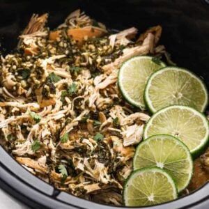 Shredded chicken topped with herbs and garnished with four slices of fresh lime, served in a black slow cooker—perfect for adding to your Meal Plan 69.