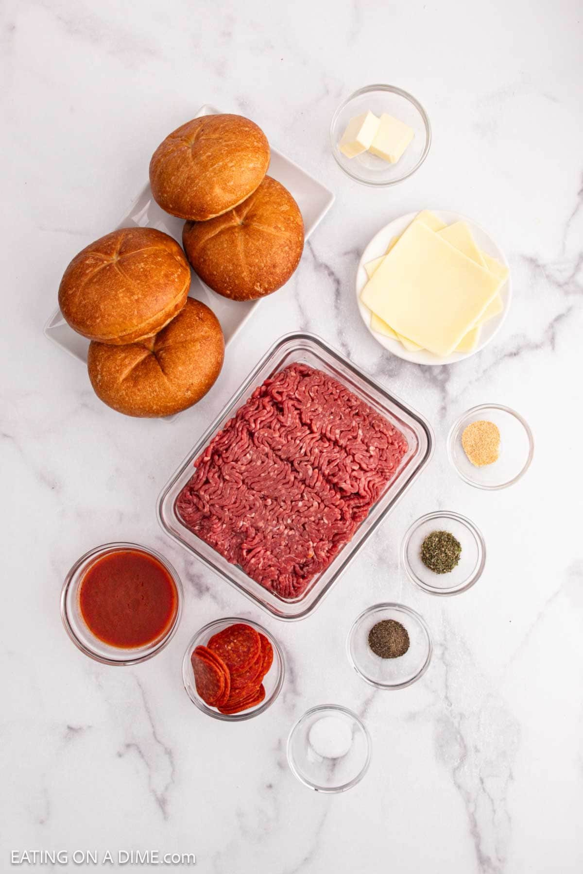 Top-down view of Pizza Burger ingredients—hamburger buns, sliced cheese, ground beef, pepperoni, tomato sauce, butter, and spices—neatly arranged on a white marble surface for a delicious recipe.