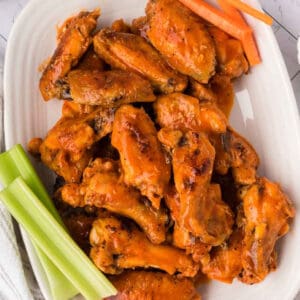 A platter of spicy baked chicken wings garnished with fresh celery and carrot sticks, served on a white dish.