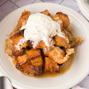 A plate of classic Bread Pudding topped with a scoop of vanilla ice cream and drizzled with caramel sauce, served on a white dish.