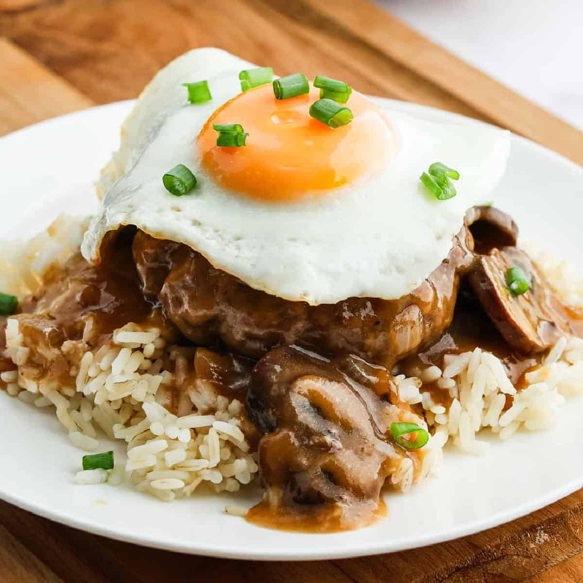 A classic Loco Moco: a plate of rice topped with a hamburger patty, savory brown gravy with mushrooms, and a sunny-side-up egg, all garnished with chopped green onions.