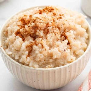 A white bowl filled with creamy Slow Cooker Rice Pudding, topped with a sprinkle of ground cinnamon.