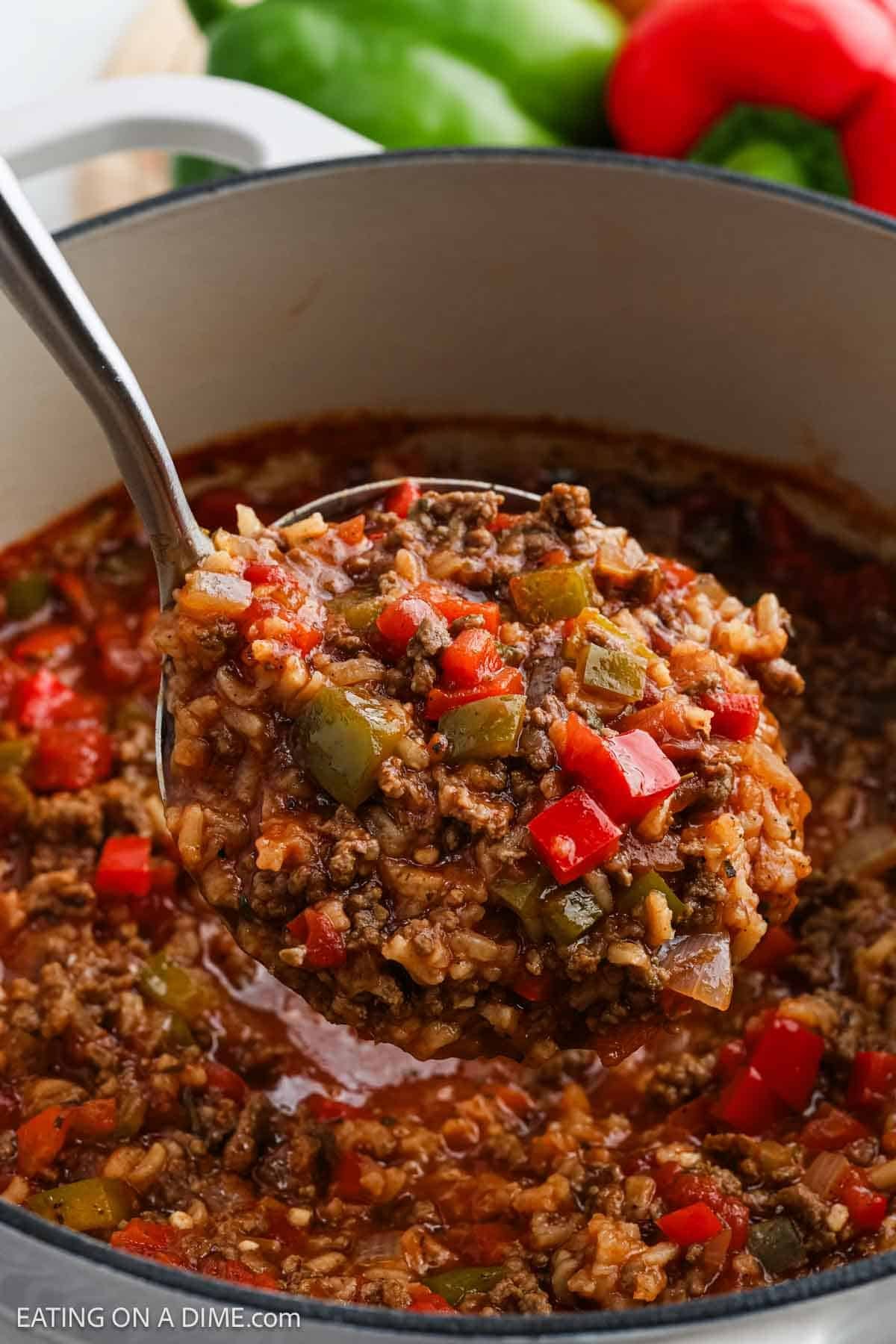 A ladle scoops up Stuffed Pepper Soupโa hearty mixture of ground beef, rice, diced red and green bell peppers, and tomato sauce. This flavorful stew boasts a rich, chunky texture and vibrant colors.