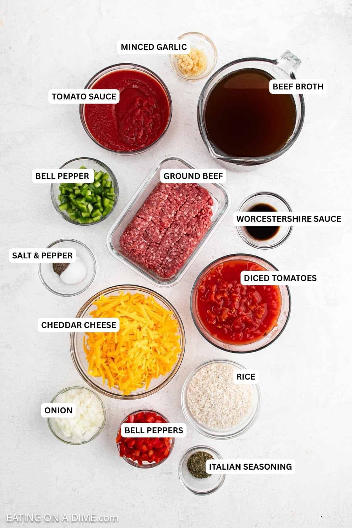 Ingredients for recipe: ground beef, shredded cheddar cheese, diced tomatoes, broth, rice, bell peppers, onions, tomato sauce, garlic, and seasonings on a white surface.