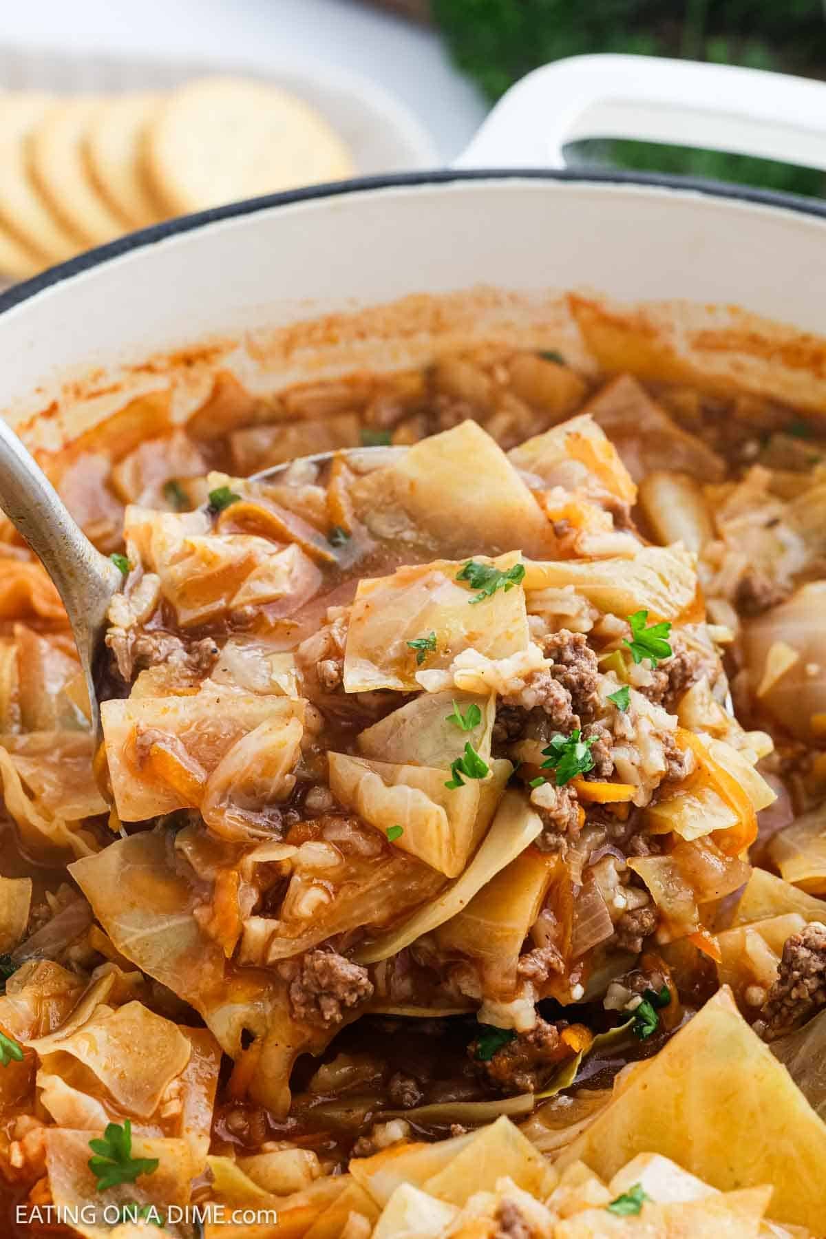 A close-up of Cabbage Roll Soup, filled with chopped cabbage, ground beef, and tomato broth. A large spoon lifts a hearty serving topped with fresh herbs, while crackers sit in the background for the perfect pairing.