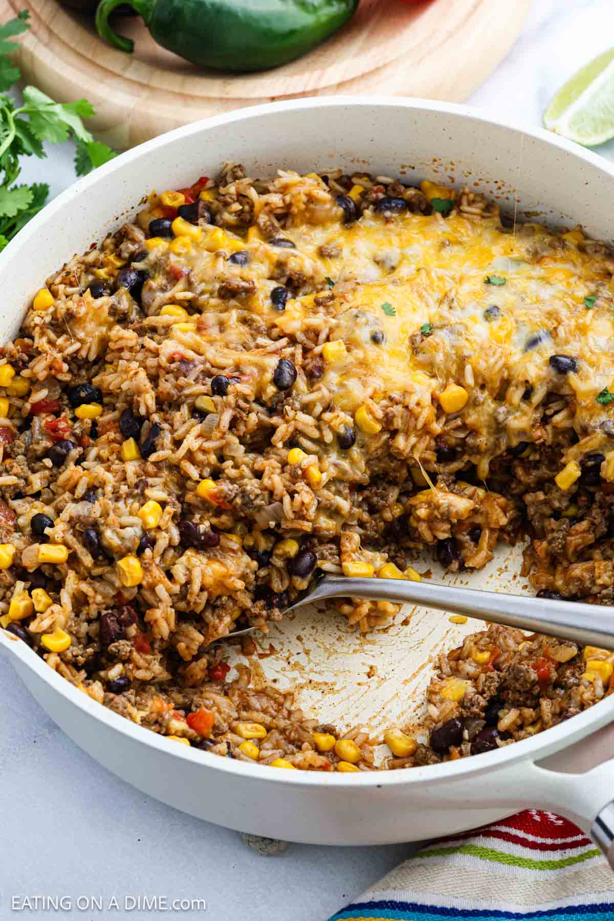 A skillet filled with a cheesy Mexican Rice Casserole, featuring rice, black beans, corn, ground meat, and melted cheese, with a serving spoon resting inside.