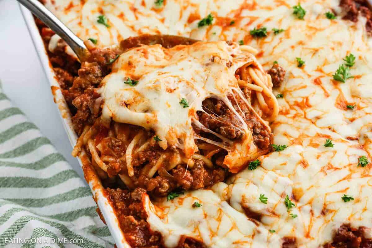 A close-up of an Alfredo Spaghetti casserole topped with melted cheese and sprinkled with herbs, with a serving being lifted out on a spatula—just like the viral TikTok recipes you’ve seen.