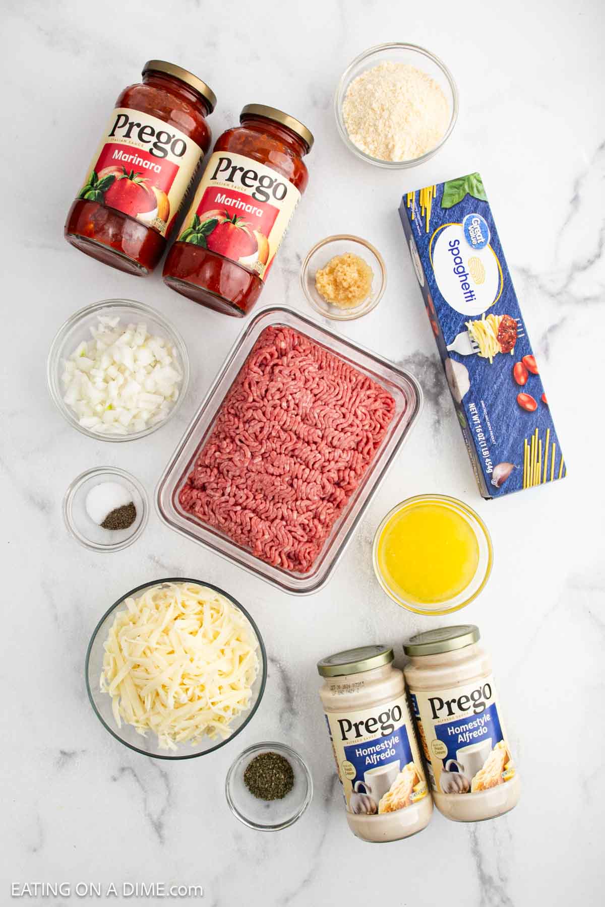 Top-down view of Alfredo Spaghetti ingredients—ground beef, marinara and Alfredo sauce, spaghetti, shredded cheese, Parmesan, onions, garlic, melted butter, salt, and pepper—perfect for recreating a viral TikTok recipe at home.