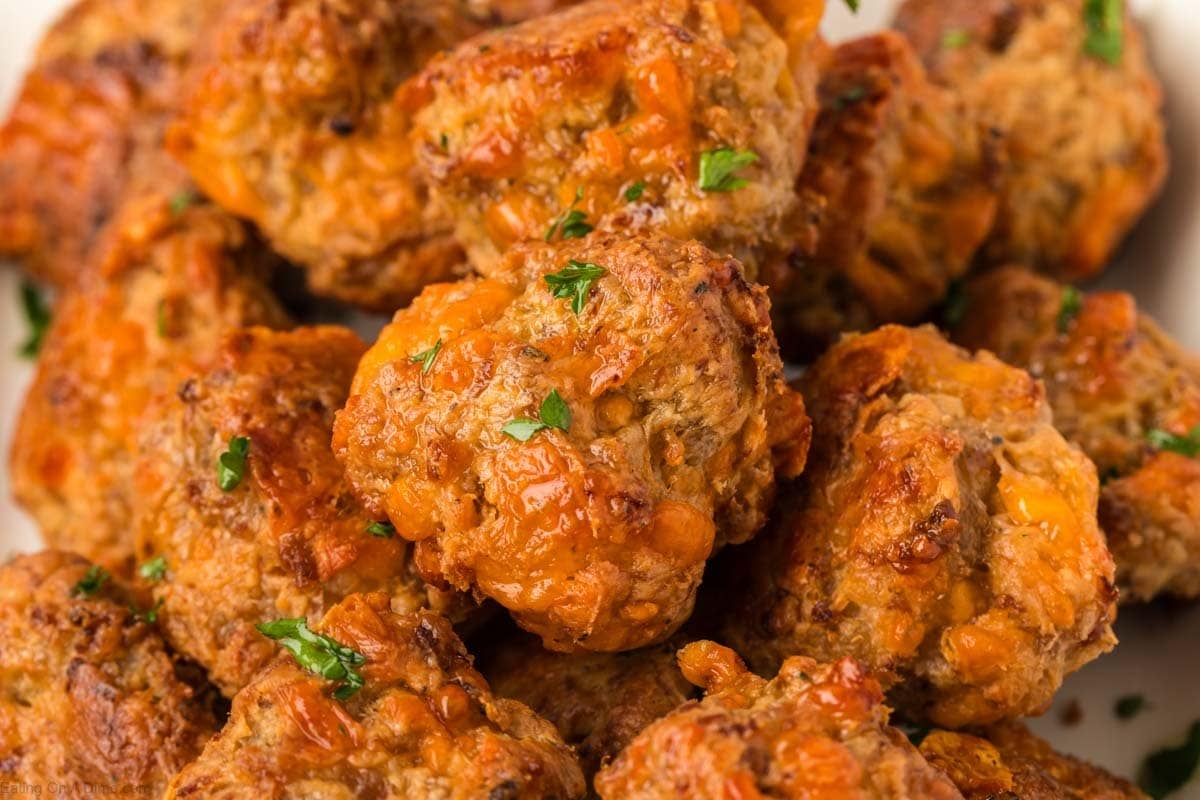A close-up of golden-brown cream cheese sausage balls with melted cheese and bits of parsley on top, piled together on a white plate.