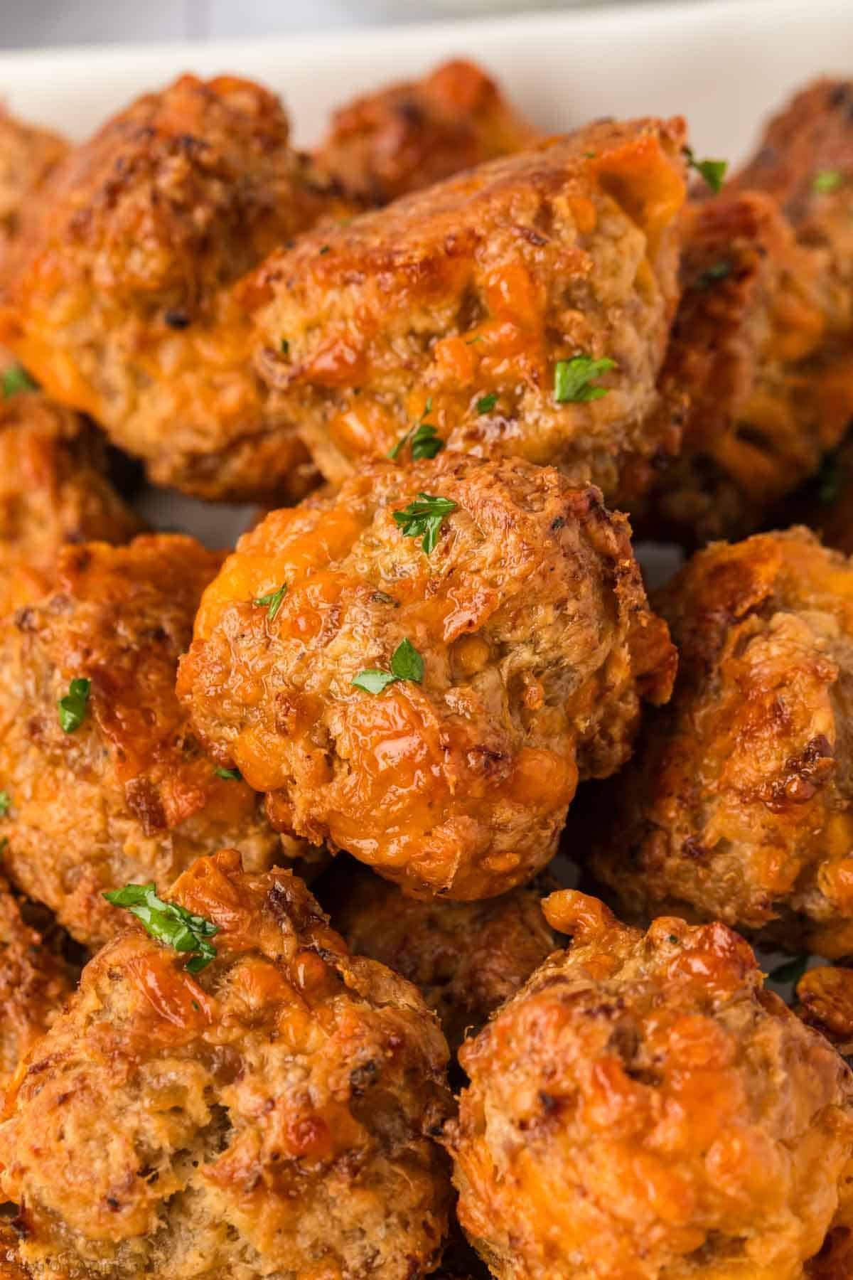 Close-up of golden-brown Cream Cheese Sausage Balls with melted cheese and sprinkled with chopped parsley, stacked on a white plate.
