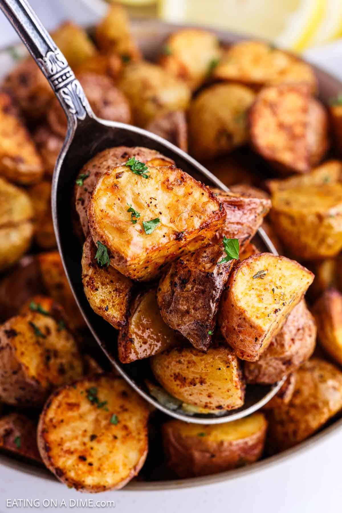 A spoonful of seasoned, air fryer potatoes garnished with fresh herbs, held above a bowl filled with more crispy roasted potatoes.