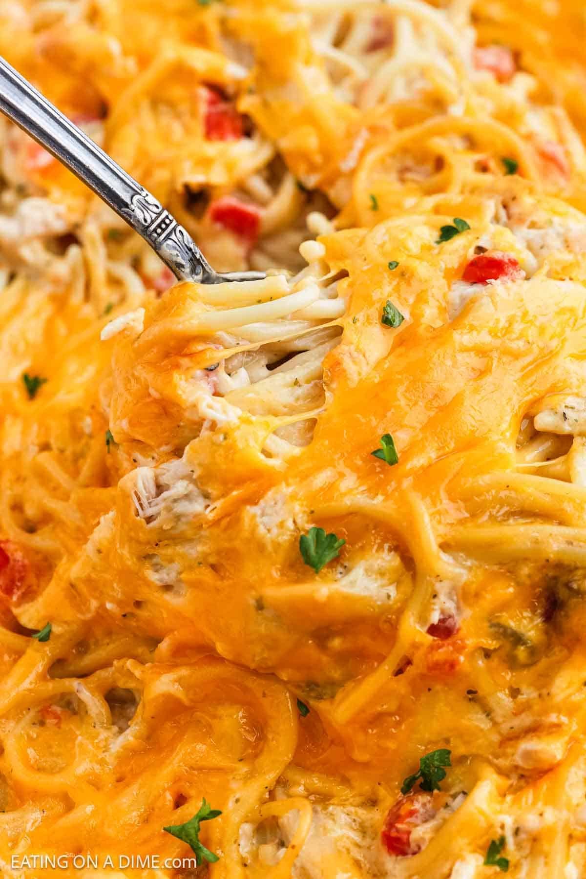 A close-up of baked chicken spaghetti, topped with melted cheddar cheese and garnished with chopped parsley, with a fork lifting a portion from the dish.