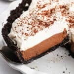A slice of chocolate cream pie with a dark cookie crust, creamy chocolate filling, and a thick layer of whipped cream, topped with chocolate shavings, is lifted from the dish—an irresistible Chocolate Cream Pie Recipe come to life.