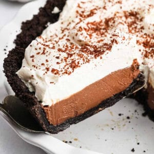 A slice of chocolate cream pie with a dark cookie crust, creamy chocolate filling, and a thick layer of whipped cream, topped with chocolate shavings, is lifted from the dish—an irresistible Chocolate Cream Pie Recipe come to life.