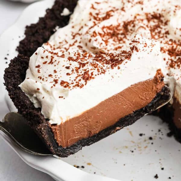 A slice of chocolate cream pie with a dark cookie crust, creamy chocolate filling, and a thick layer of whipped cream, topped with chocolate shavings, is lifted from the dish—an irresistible Chocolate Cream Pie Recipe come to life.