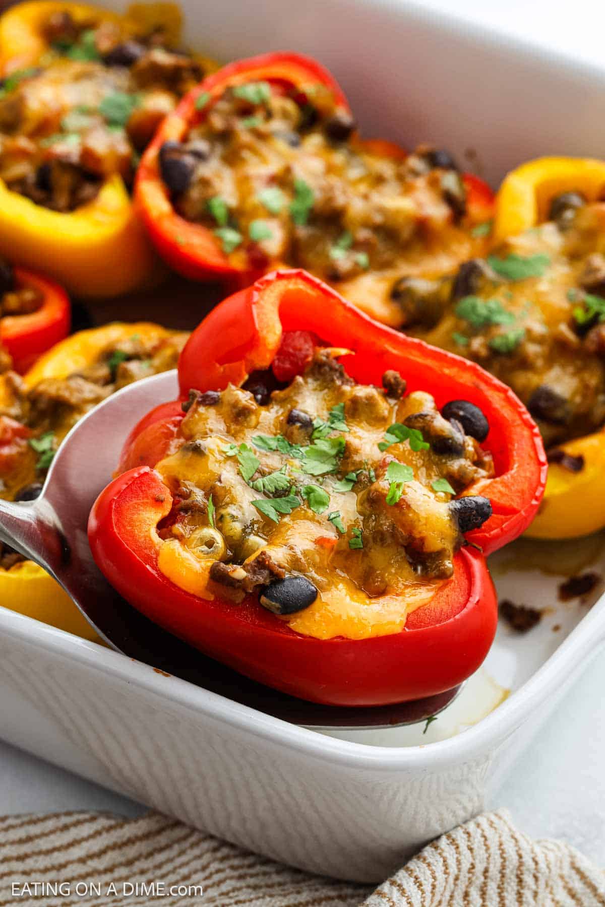 A close-up of Taco Stuffed Peppers filled with a savory mixture of ground meat, black beans, and melted cheese, garnished with chopped herbs in a white baking dish alongside other stuffed peppers.