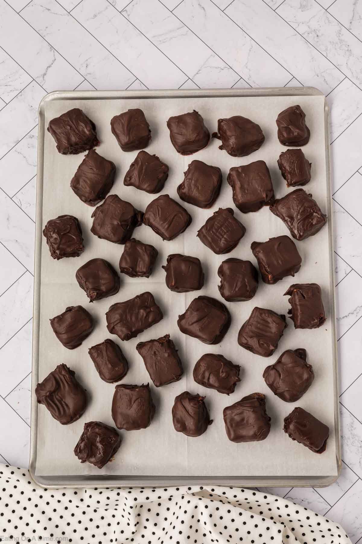 A baking sheet lined with parchment paper holds several square-shaped Cool Whip Candy treats, neatly arranged in rows. The background features a white and gray tiled surface.