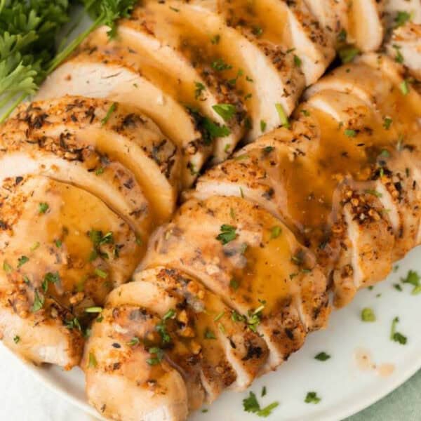 Sliced, seasoned cooked chicken breast topped with brown gravy and garnished with chopped parsley, served on a white plate—similar to slow cooker turkey breast—for a hearty and comforting meal.