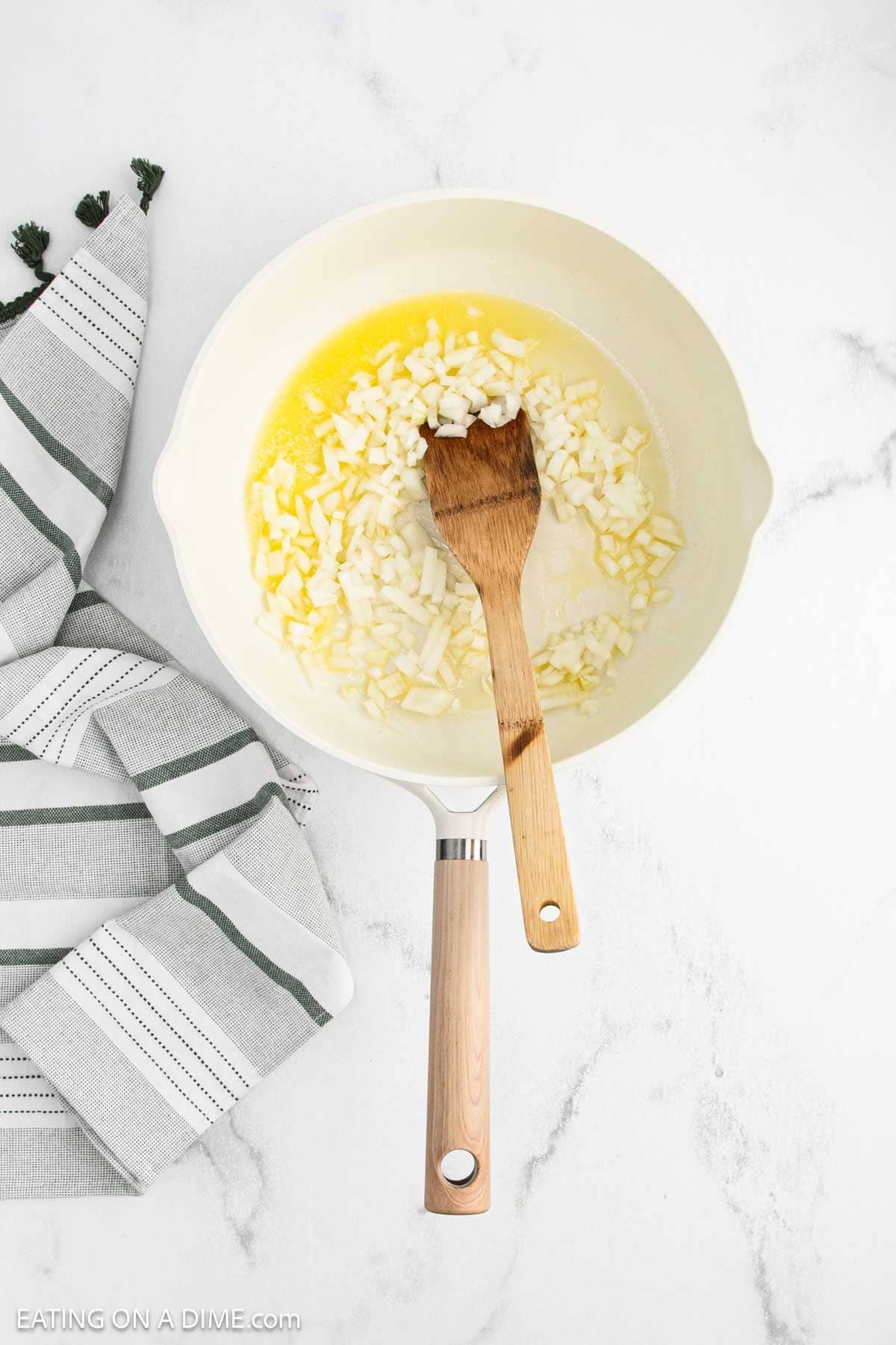 A white skillet with chopped onions cooking in butter.