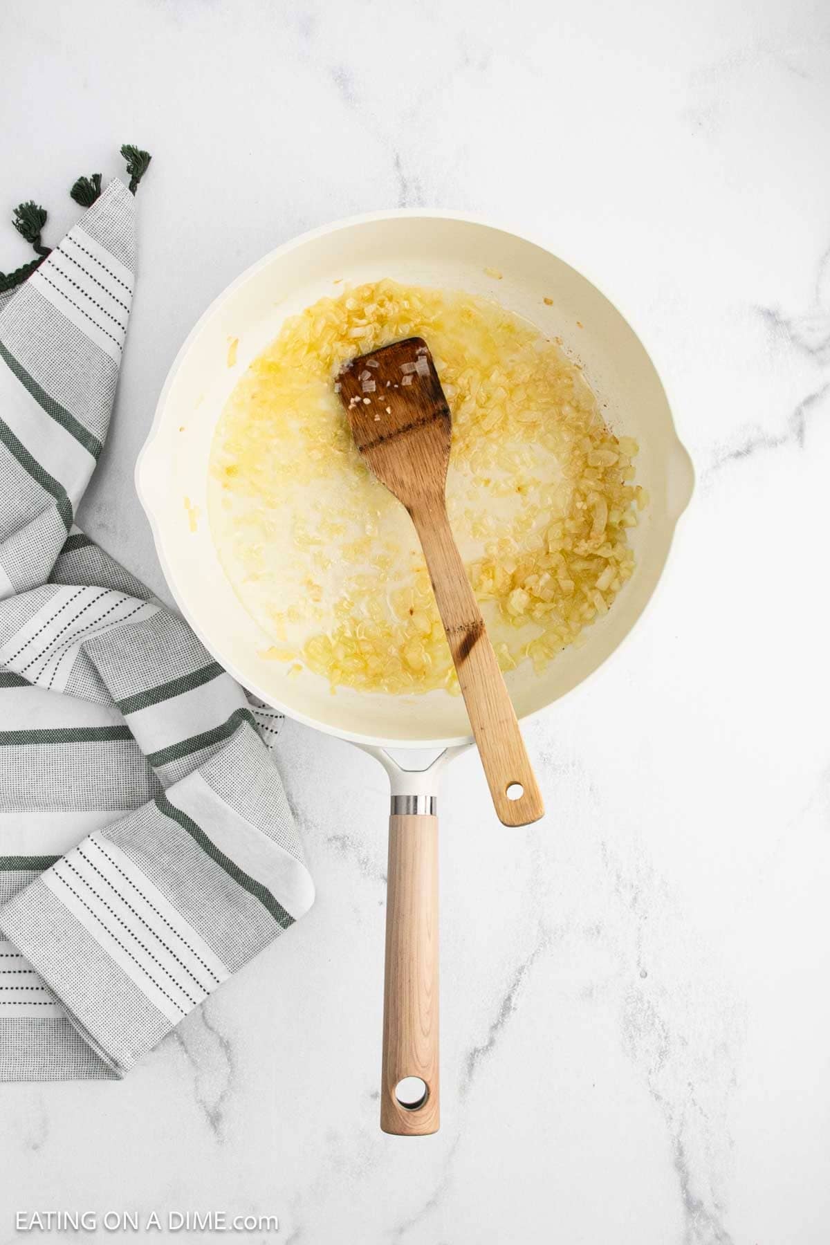 A white skillet with sautéed chopped onions and melted butter.