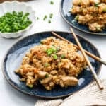 A plate of Teriyaki Chicken Rice with vegetables and green onions, garnished with chopped scallions. A pair of chopsticks rests on the plate, with a bowl of more green onions in the background.